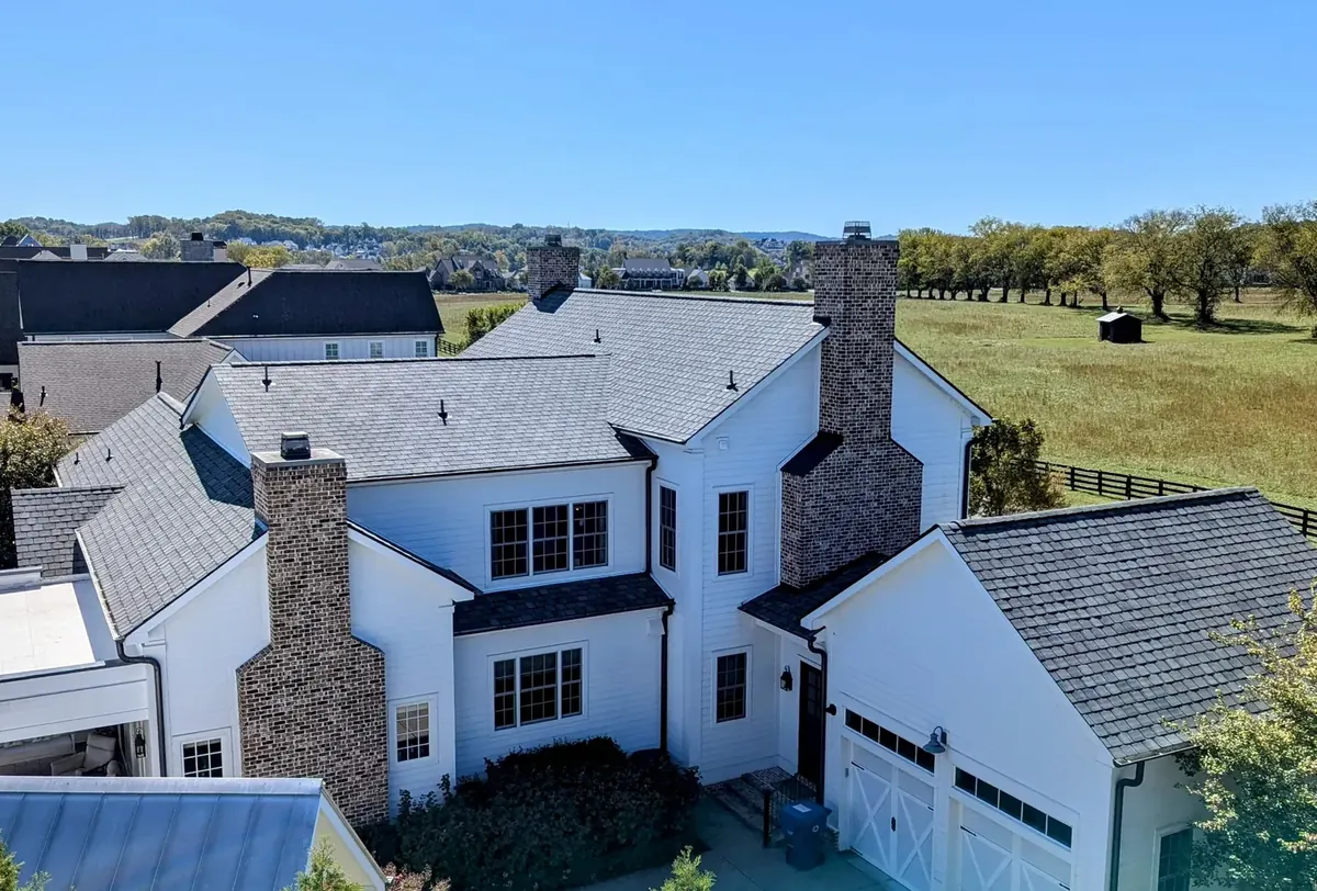 New architectural shingle roof on a white farmhouse with brick chimneys